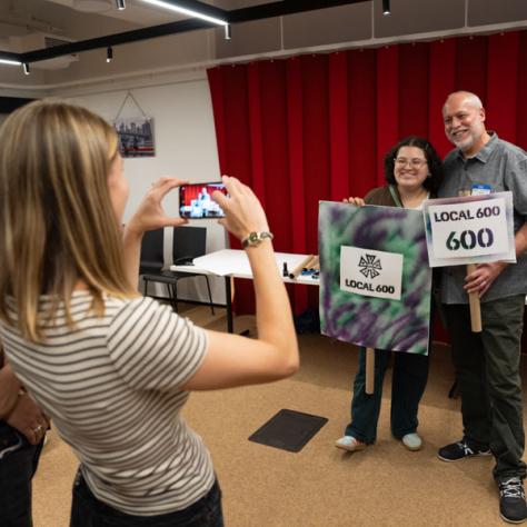 Photo of woman taking a photo of two people holding signs. 