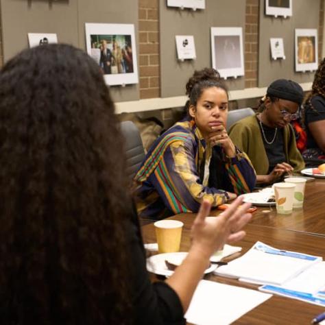 People at table watching woman speak at the head of the table. 