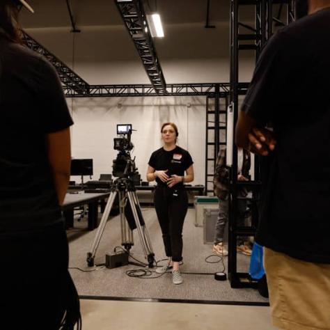 People watching a woman next to a camera. 