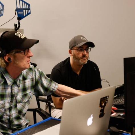 Two men sitting with laptops at a table. 