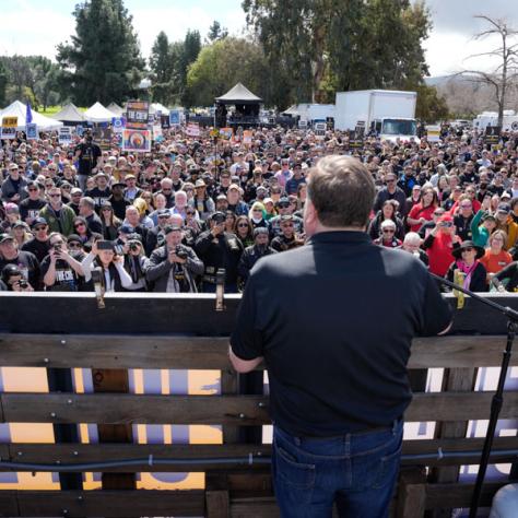 Man speaking to large crowd of people at rally. 