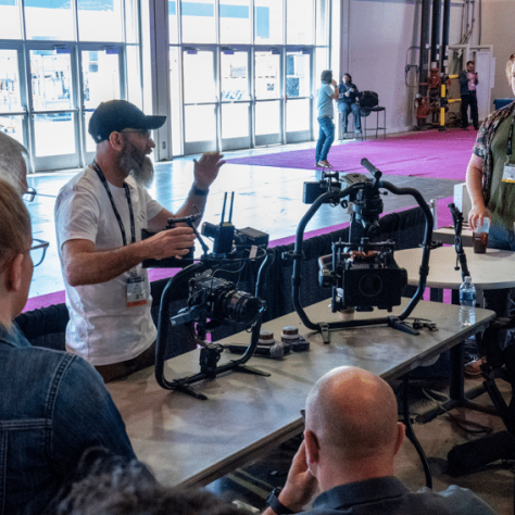 People standing around table with equipment while man speaks. 