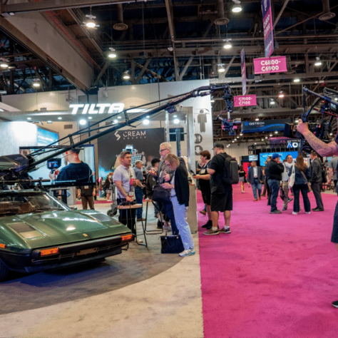 People in exhibit hall in front of green car with camera equipment on it. 
