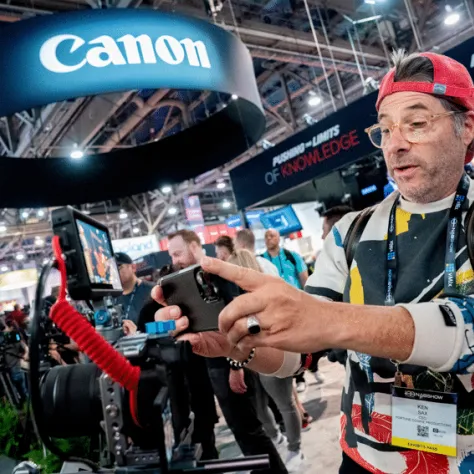 Man with red hat pointing to camera in exhibit hall. 