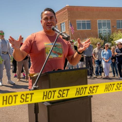 Man speaking into microphone with yellow tape in front of him.