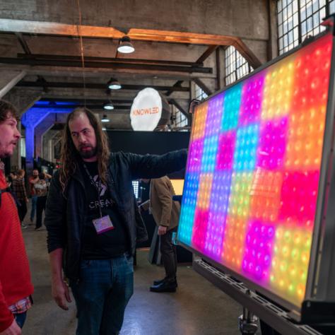 Photo of people in front of light up color board. 