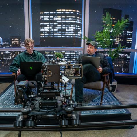 Two people sitting on a dais in front of a camera. 