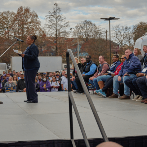 Person on stage speaking while people watch. 