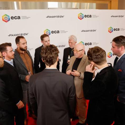 People standing on red carpet in a circle talking. 