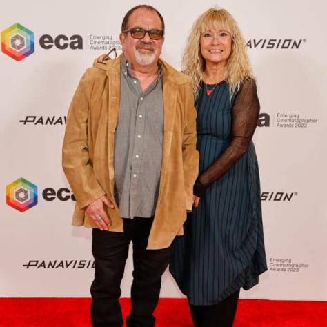 Two people posing for photo in front of backdrop. 