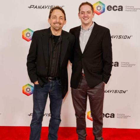 Two people posing for photo in front of backdrop. 