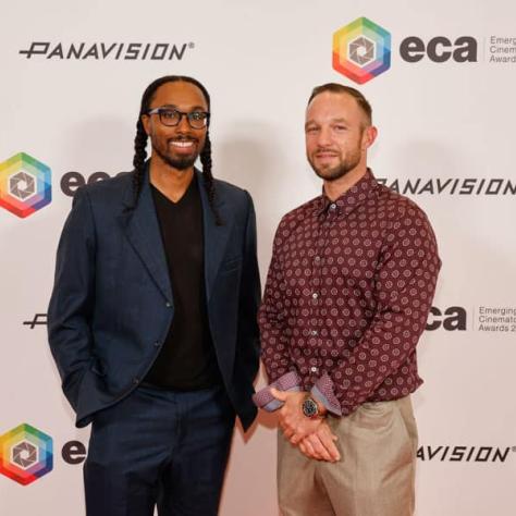 Two people posing for photo in front of backdrop. 