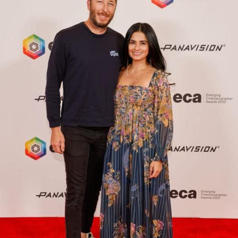 Two people posing for photo in front of backdrop. 