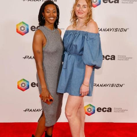 Two people posing for photo in front of backdrop. 
