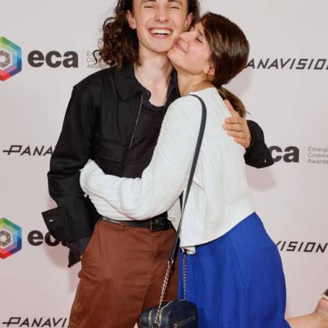 Two people posing for photo in front of backdrop. 