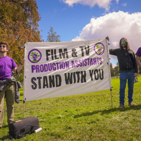 Group of people posing for photo with large sign. 