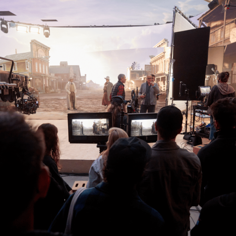 People watching screens and someone on a set. 