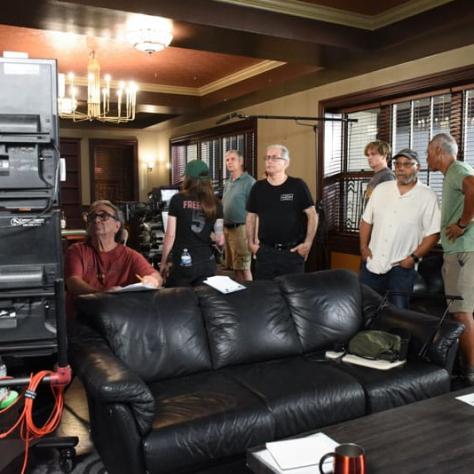 People standing behind a couch looking at something. 