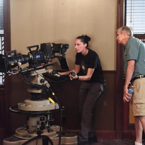 Woman working behind a camera with man watching. 