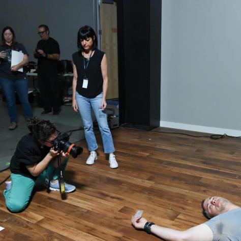 Woman sitting on floor taking photo of man lying on the ground while woman watches. 