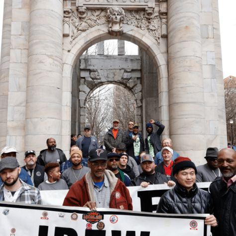 People outside of arch holding signs. 
