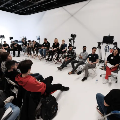 View of audience and people sitting in chairs at the front of the room. 