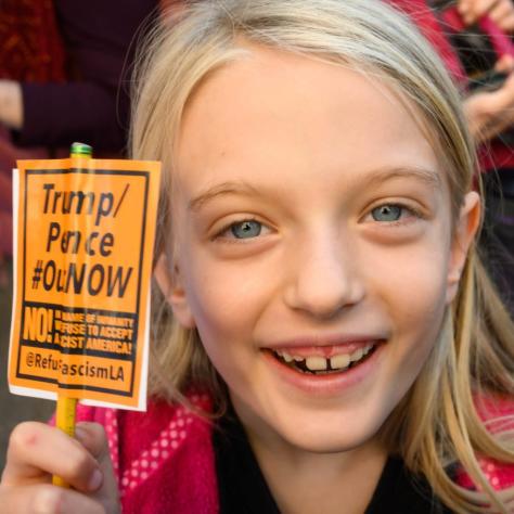 Young girl holding a small sign that reads "Trump/Pence #OutNow"