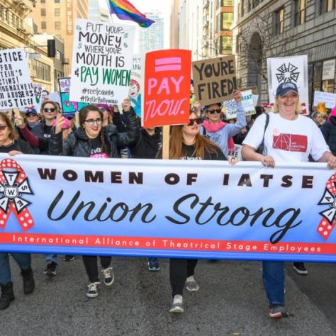 People marching while holding signs and a banner