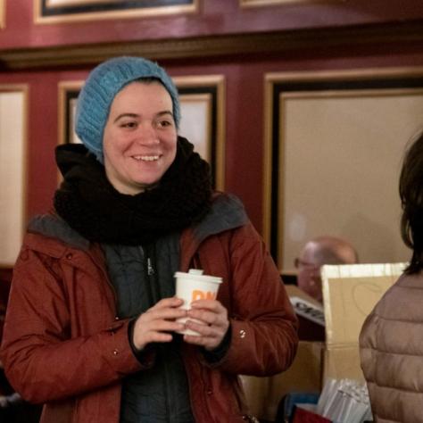 Woman smiling wearing cold weather clothes holding a cup of coffee indoors
