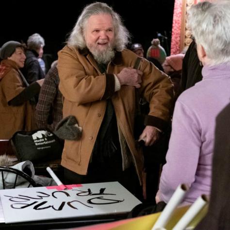 Man stands with a sign resting on a table