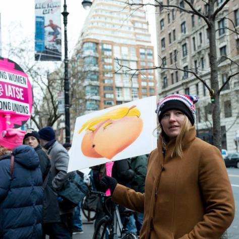 Woman holds sign that shows a peach that looks like a butt and also Trump's face