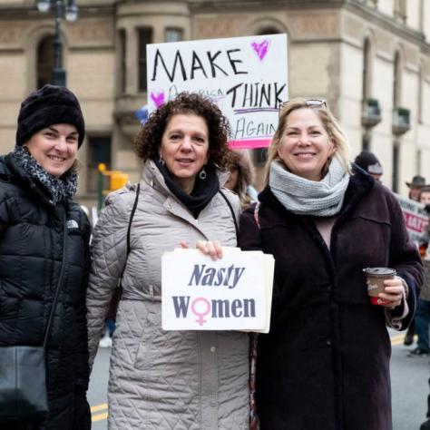 Woman holding a sign that reads "Nasty women" where the "o" has been replaced with the female symbol