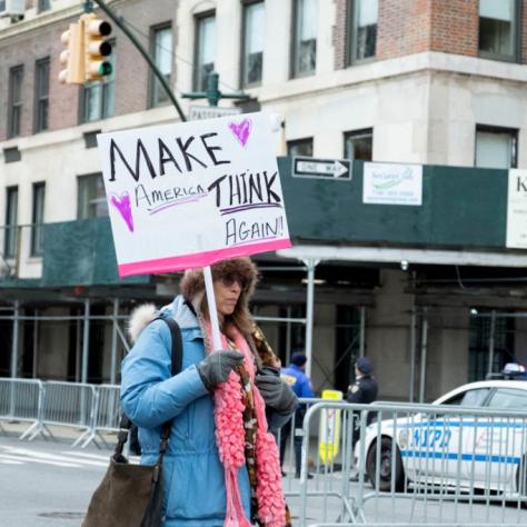 Woman holding sign that reads "MAKE AMERICA THINK AGAIN!!"