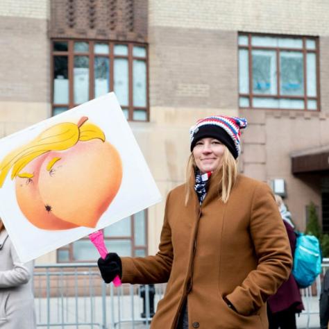 Woman holding a sign that's a peach that looks like a butt but also Trump