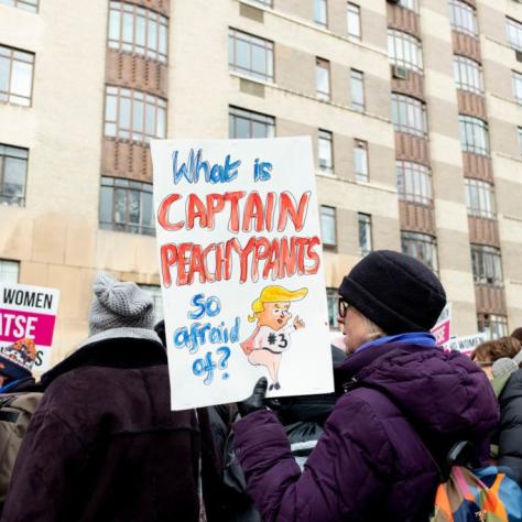 Woman holding a sign in a crowd that reads "What is CAPTAIN PEACHYPANTS so afraid of?"