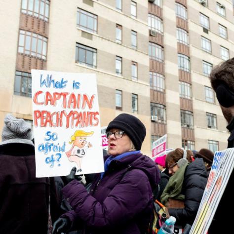 Woman holding a sign in a crowd that reads "What is CAPTAIN PEACHYPANTS so afraid of?"