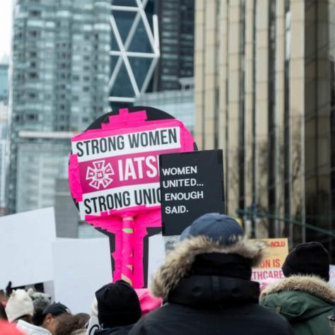 Sign that reads "STRONG WOMEN STRONG UNIONS IATSE" and another that reads "WOMEN UNITED... ENOUGH SAID"