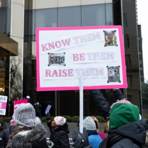 Woman holding sign that reads "KNOW THEM BE THEM RAISE THEM"