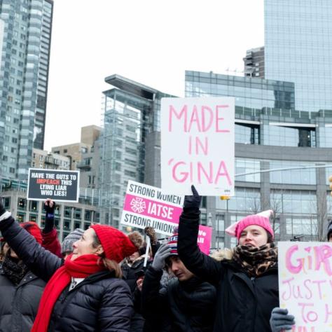 People marching while holding signs with one that reads "MADE IN 'GINA"