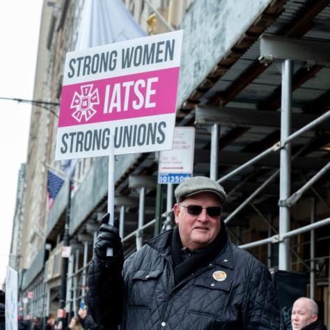 Man holding sign that reads "STRONG WOMEN STRONG UNIONS IATSE"