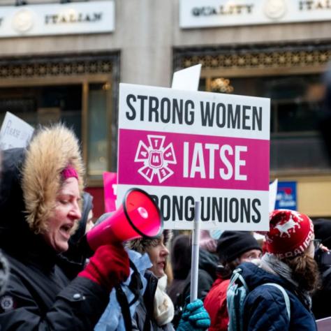 People marching while holding signs with a woman speaking into a megaphone