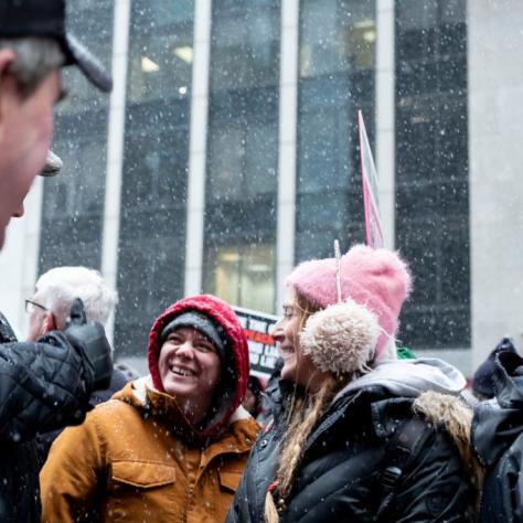 People marching while holding signs with snow starting to fall