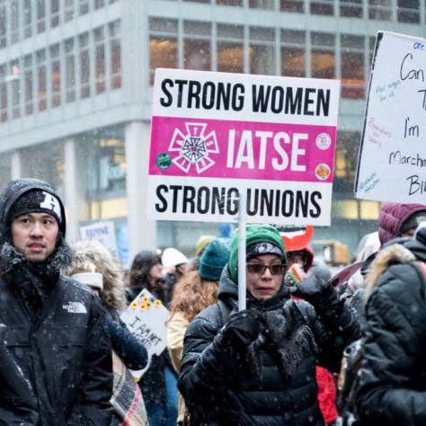 People marching while holding signs with snow falling
