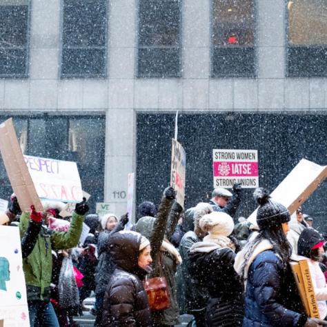 People marching while holding signs with snow falling