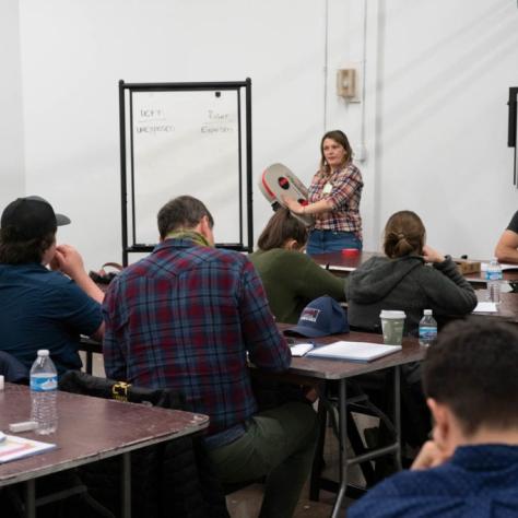A woman shows a film loader to a classroom of students
