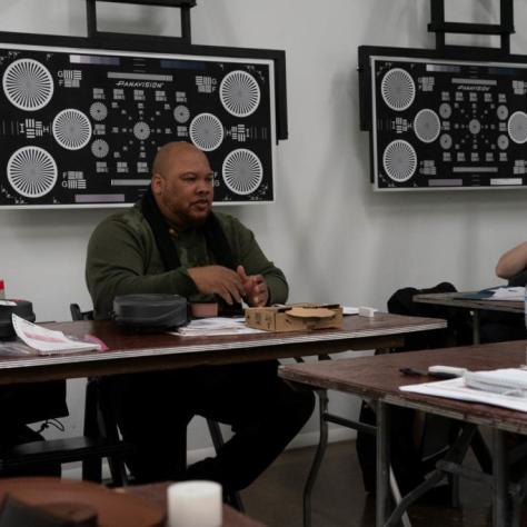 A man seated at a table speaks as another man listens