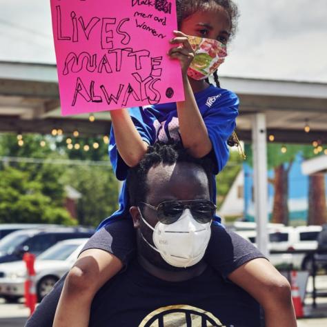 Child holding a sign sits on man's shoulders