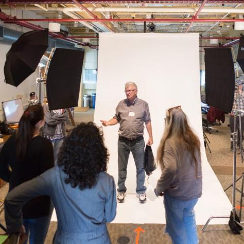 Man stands in front of a backgrop facing a group of people