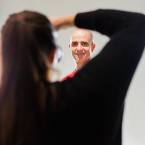 Woman points a camera at a man standing in front of a backdrop