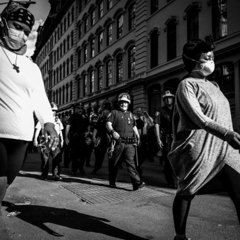 Two women walking in the street with police officers behind them